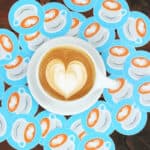 Coffee cup with heart latte art surrounded by stickers with heart latte art.
