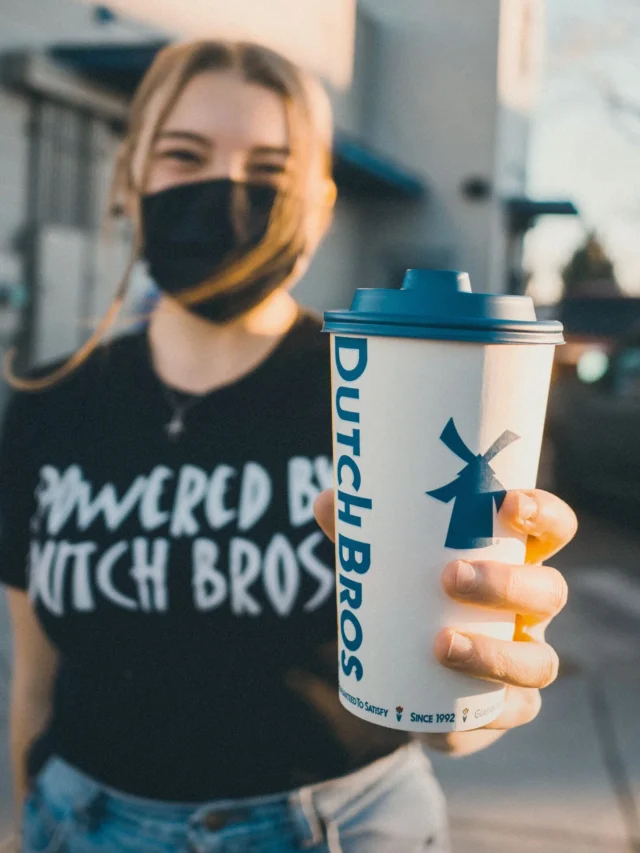 Dutch Bros worker with hand extended giving viewer a Dutch Bros cup