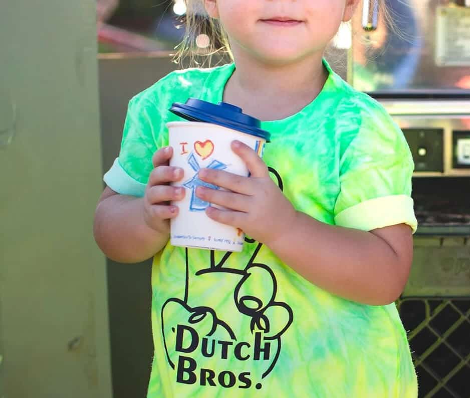 Kid holding a kids Dutch Bros cup and wearing a tie dyed Dutch Bros shirt.
