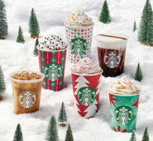 Starbucks 2022 holiday featured drinks sitting largely in snow surrounded by Christmas trees.