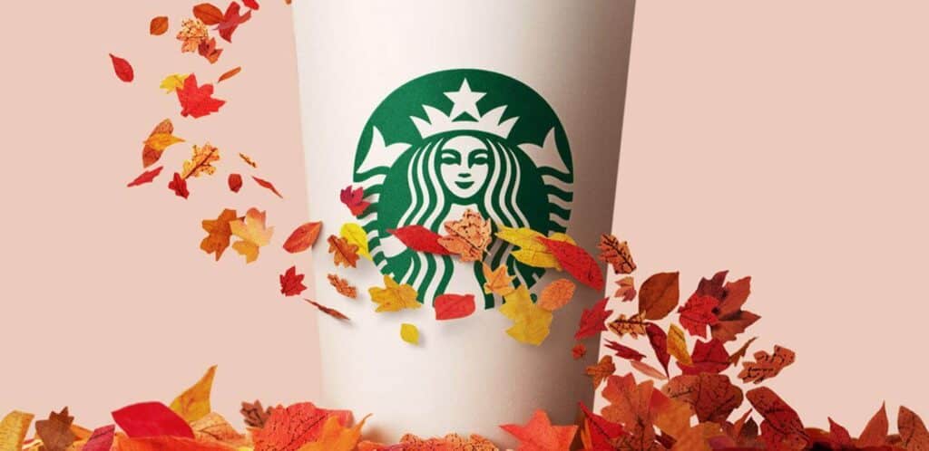 Starbucks cup with autumn leaves blowing in front.