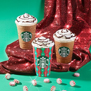 Three Starbucks holiday drinks with red sparkling fabric surrounding them.
