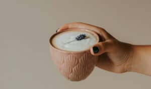 A coffee mug held by hand showing a latte with a sprig of lavender on top.